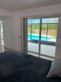 A bedroom features a dark bed and a sliding glass door overlooking a screened-in pool — 4026 TENITA DRIVE, WINTER PARK, FL