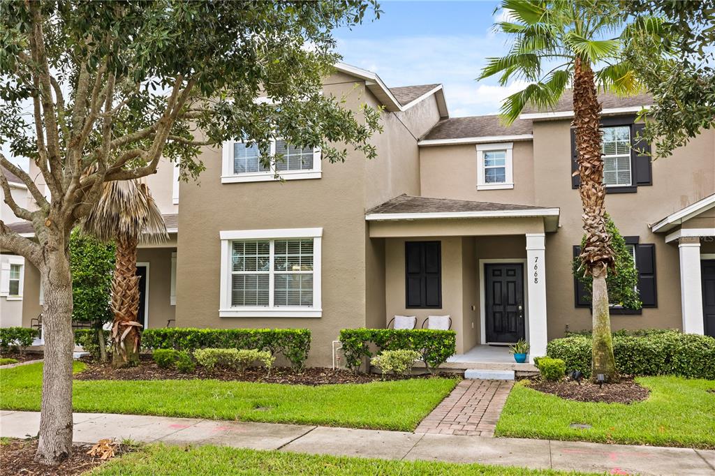A two-story tan townhouse features a covered entryway, dark shutters, and a palm tree — 7668 FAIRGROVE AVENUE, WINDERMERE, FL