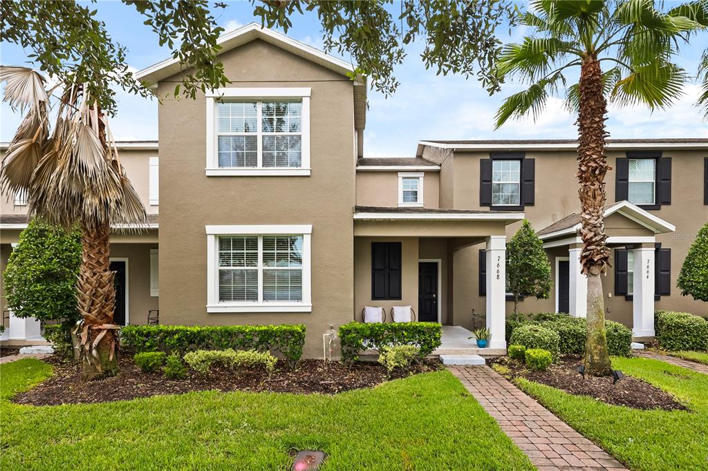 A two-story townhouse exterior features tan stucco walls, white trim, and a brick walkway — 7668 FAIRGROVE AVENUE, WINDERMERE, FL