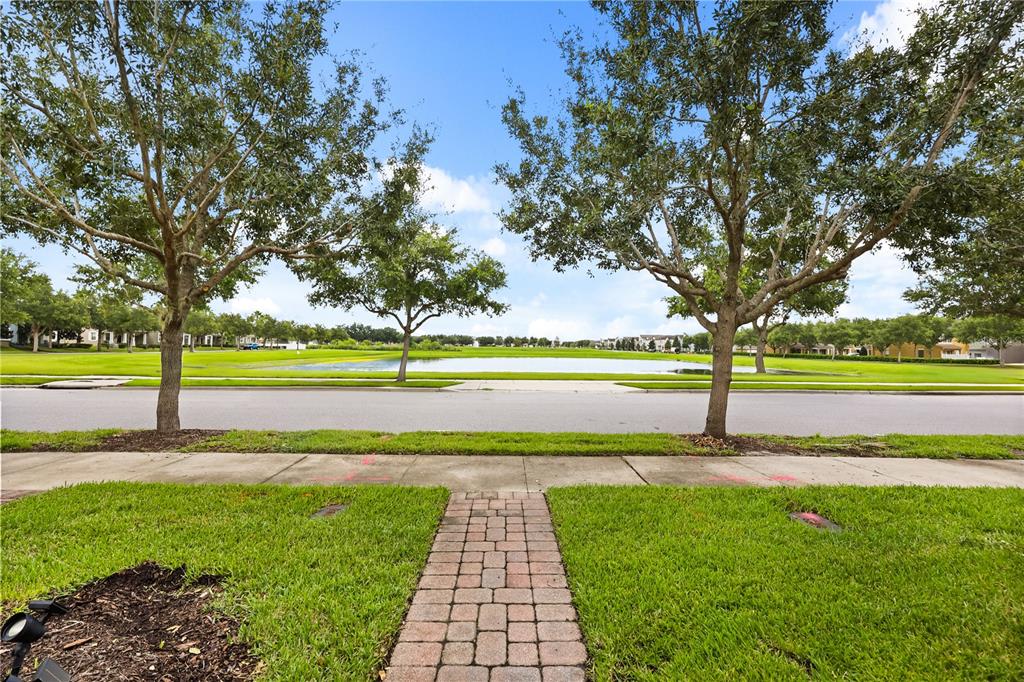 A paved walkway leads through a grassy yard toward a street and a small pond — 7668 FAIRGROVE AVENUE, WINDERMERE, FL