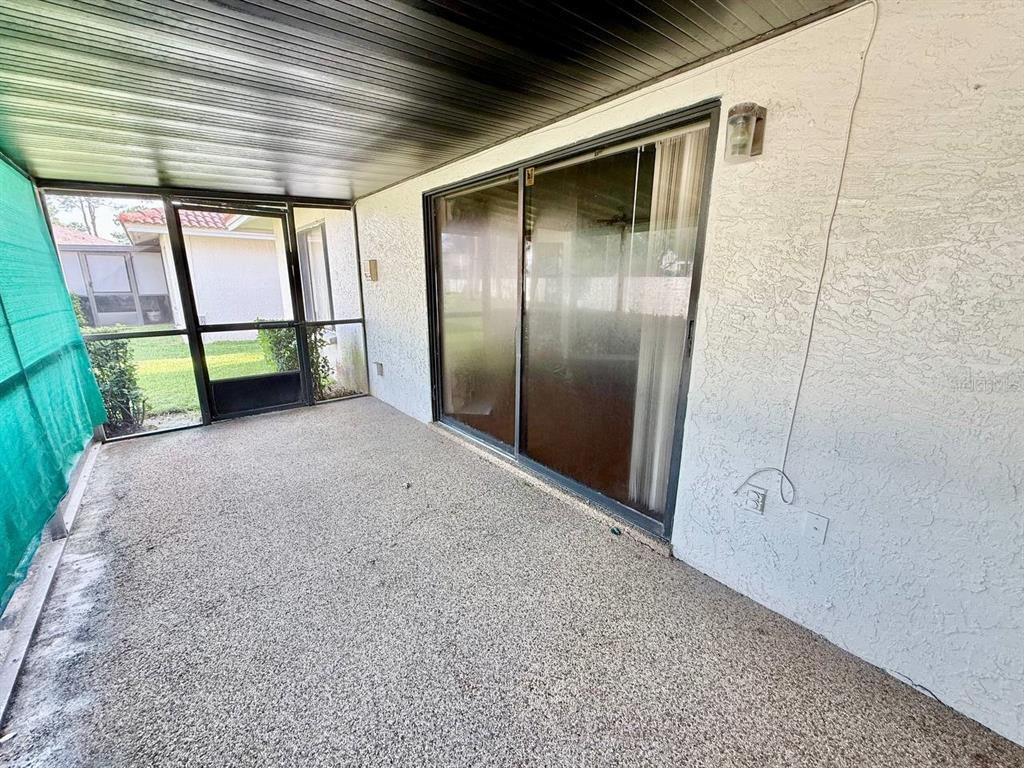 A covered patio with a textured concrete floor, sliding glass doors, and a screened enclosure — 18308 AINTREE COURT, TAMPA, FL