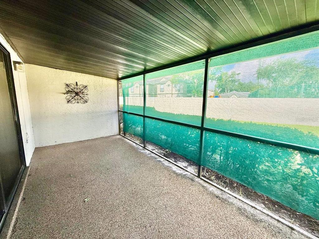 A covered patio with a textured concrete floor, white walls, and green privacy screening — 18308 AINTREE COURT, TAMPA, FL