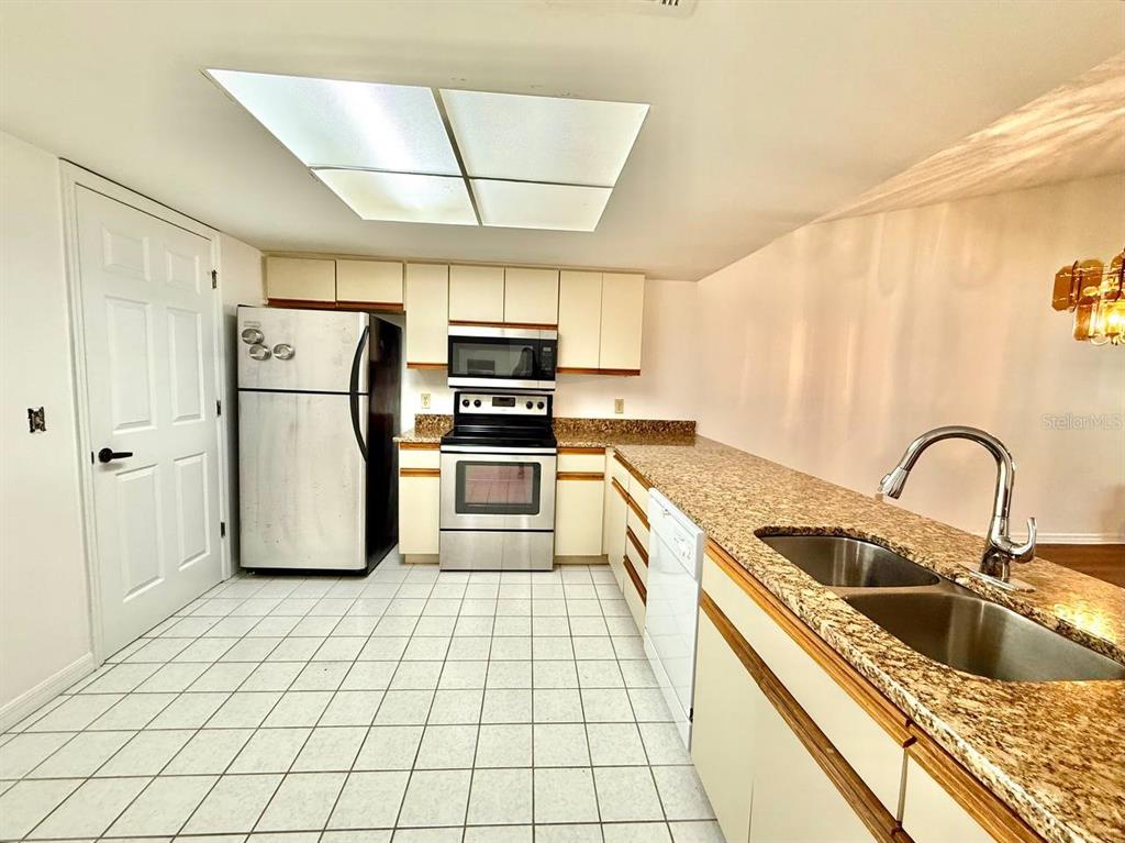 A kitchen features white cabinets, granite countertops, stainless steel appliances, and white tile flooring — 18308 AINTREE COURT, TAMPA, FL