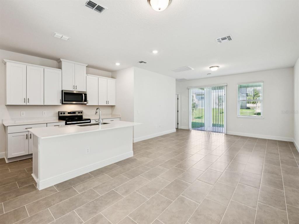 A kitchen with white cabinets, a central island, and tile flooring opens to a living area — 2194 WILDBERRY WAY, MINNEOLA, FL