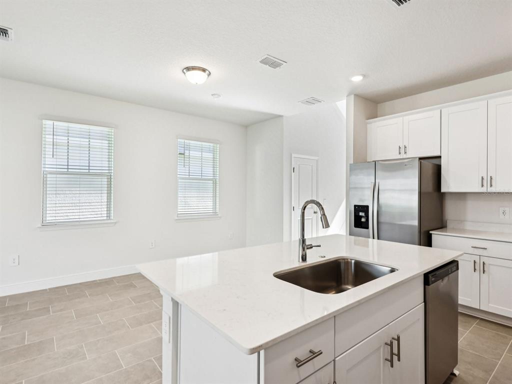 A kitchen with a white quartz island, stainless steel sink, and white cabinetry — 2194 WILDBERRY WAY, MINNEOLA, FL