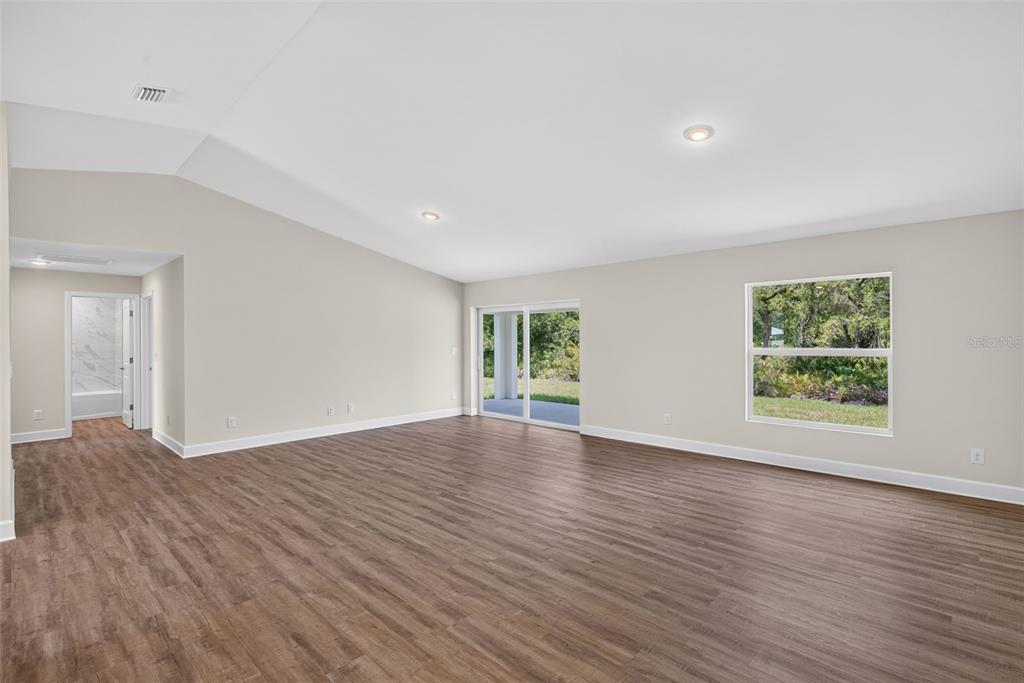 An empty living room with wood-look flooring, vaulted ceilings, recessed lighting, and a sliding glass door — 151 KIRBY STREET, PORT CHARLOTTE, FL