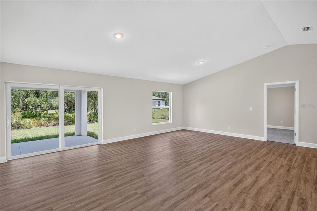 A spacious living room features vaulted ceilings, wood-look flooring, sliding glass doors, and a window — 151 KIRBY STREET, PORT CHARLOTTE, FL