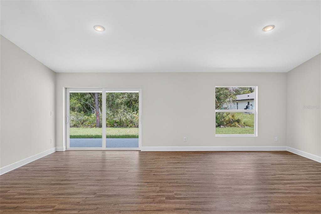 An empty room with light-colored walls, wood-look flooring, a sliding glass door, and one window — 151 KIRBY STREET, PORT CHARLOTTE, FL