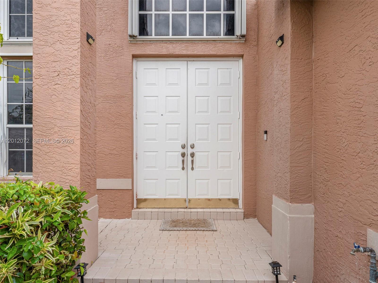 A double white front door with brass kickplates is set into a textured peach-colored wall — 16455 SW 20th St, Miramar FL 33027, MIRAMAR, FL