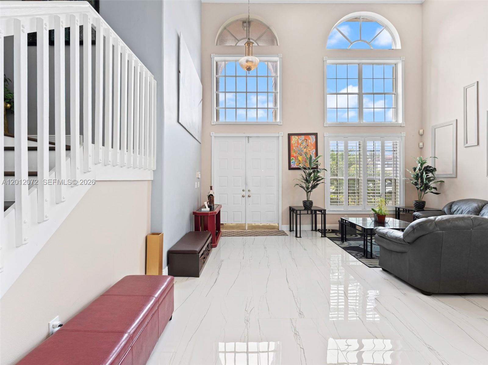 A high-ceilinged foyer features white marble floors, a staircase, and large arched windows — 16455 SW 20th St, Miramar FL 33027, MIRAMAR, FL