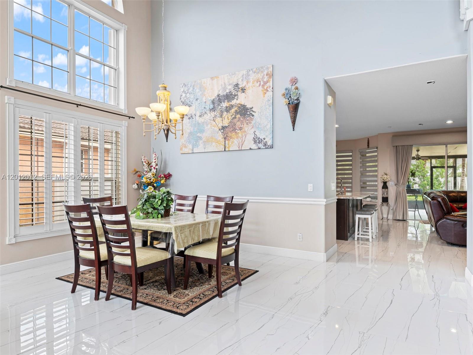 A dining area with a chandelier, table, chairs, and marble floors opens into a kitchen — 16455 SW 20th St, Miramar FL 33027, MIRAMAR, FL