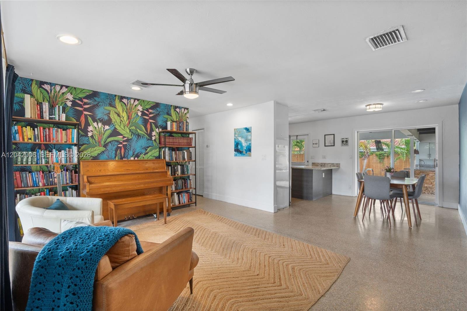 A living room features a piano, bookshelves, tropical wallpaper, and a dining area with patio access — 1250 NE 23rd Pl, Pompano Beach FL 33064, POMPANO BEACH, FL