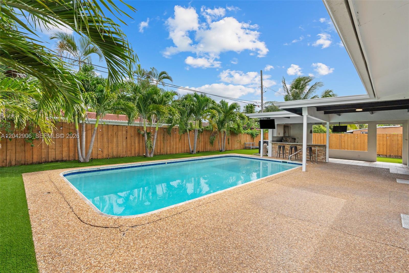 A backyard features a rectangular swimming pool, a covered patio with a bar, and palm trees — 1250 NE 23rd Pl, Pompano Beach FL 33064, POMPANO BEACH, FL
