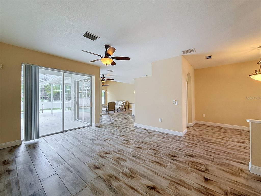 An open-concept living area features wood-look tile flooring, ceiling fans, and sliding glass patio doors — 859 INVERRY DRIVE, OLDSMAR, FL
