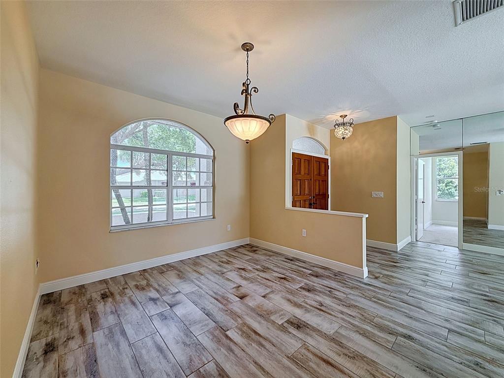 A dining room features wood-look tile flooring, a large arched window, and two hanging chandeliers — 859 INVERRY DRIVE, OLDSMAR, FL