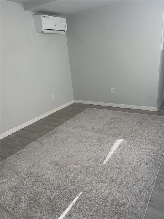 A room with gray walls, wood-look flooring, a large gray area rug, and a wall-mounted AC — 1106 50TH AVENUE DRIVE W, BRADENTON, FL