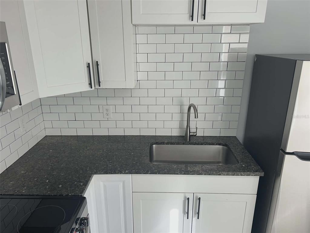 A kitchen features white cabinets, a dark granite countertop, a stainless steel sink, and subway tile — 1106 50TH AVENUE DRIVE W, BRADENTON, FL