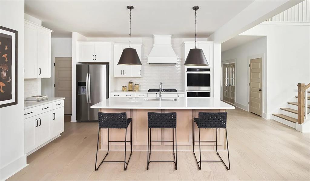 A modern kitchen features white cabinets, a large central island, and light wood flooring — 2672 VERONA LANE, ODESSA, FL
