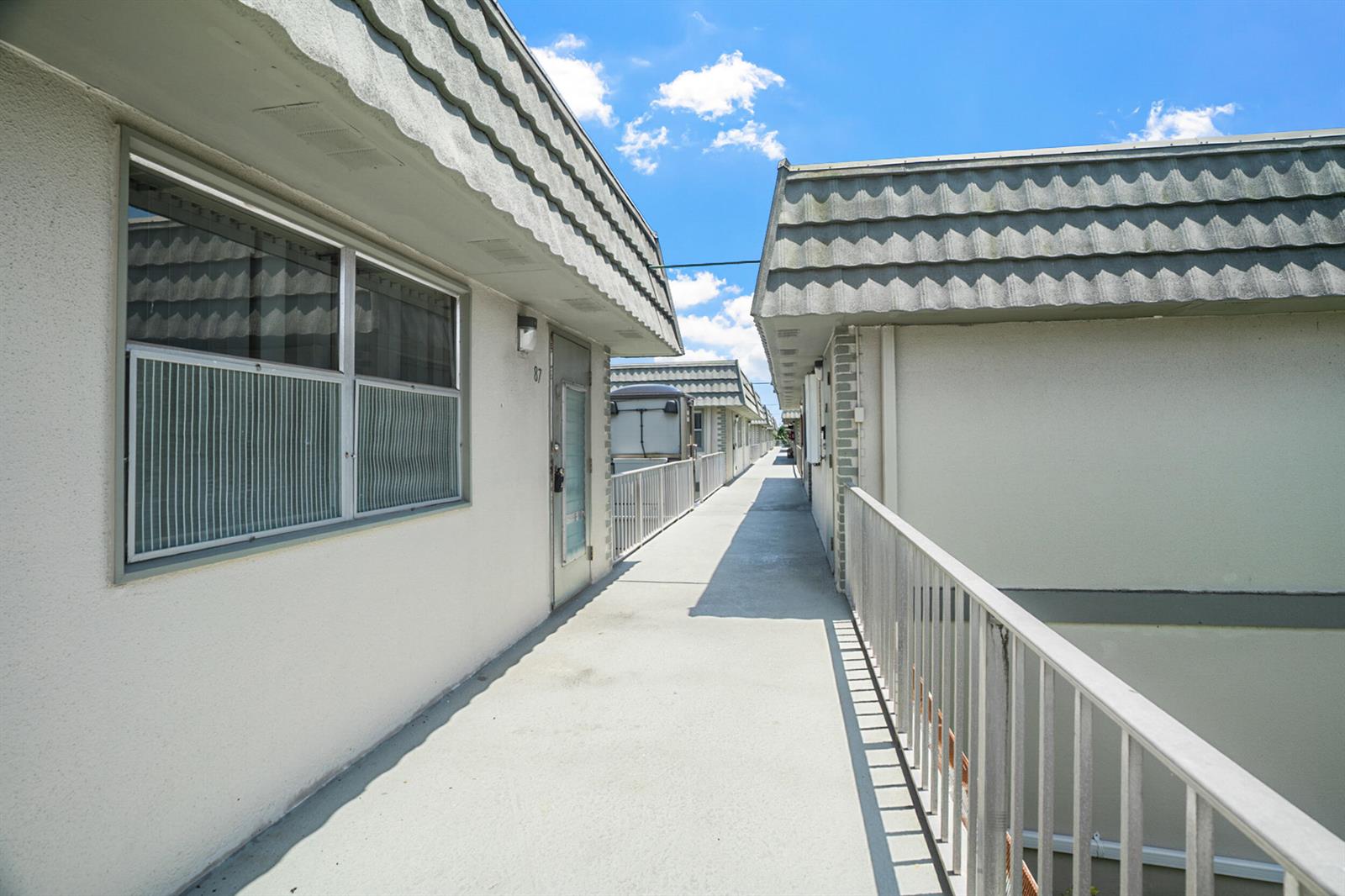 An exterior walkway between two apartment buildings with white walls and gray shingled rooflines — 87 Brittany B Avenue # B, Delray Beach FL 33446, DELRAY BEACH, FL