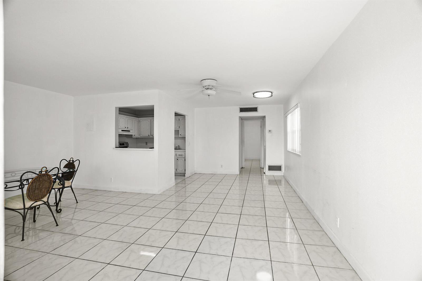 An open-concept dining area with white walls, white tile flooring, and a kitchen pass-through window — 87 Brittany B Avenue # B, Delray Beach FL 33446, DELRAY BEACH, FL
