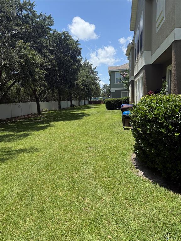 A grassy side yard runs between a multi-story house and a white privacy fence — 1993 ESTANCIA CIRCLE UNIT B, KISSIMMEE, FL