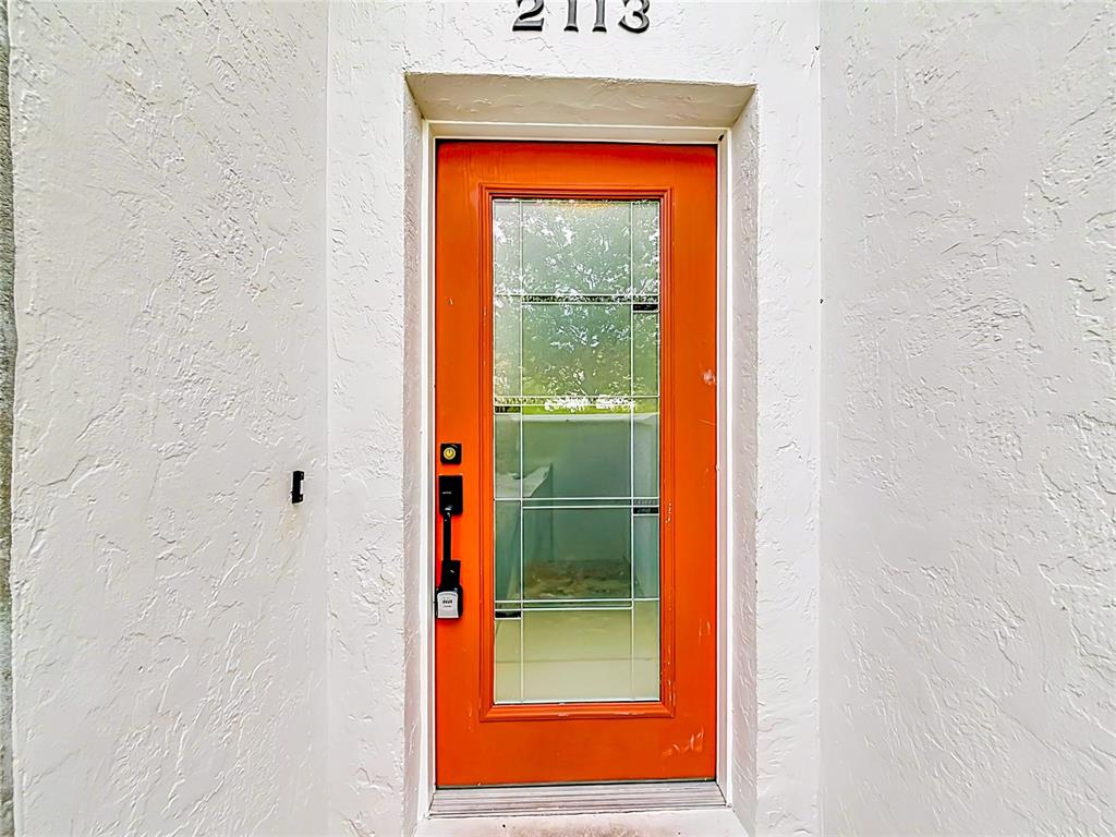 A bright orange front door with a glass panel is set into a white stucco wall — 2113 NE 38TH AVENUE, OCALA, FL