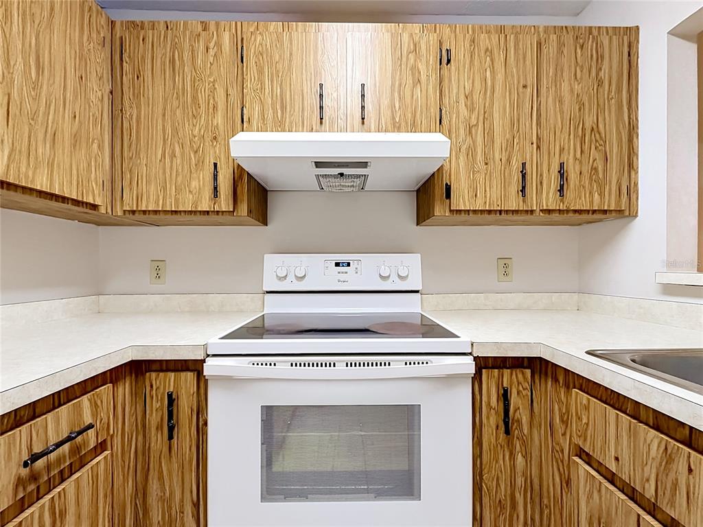 A kitchen features wood-grain cabinets, a white electric stove, and light-colored laminate countertops — 2113 NE 38TH AVENUE, OCALA, FL