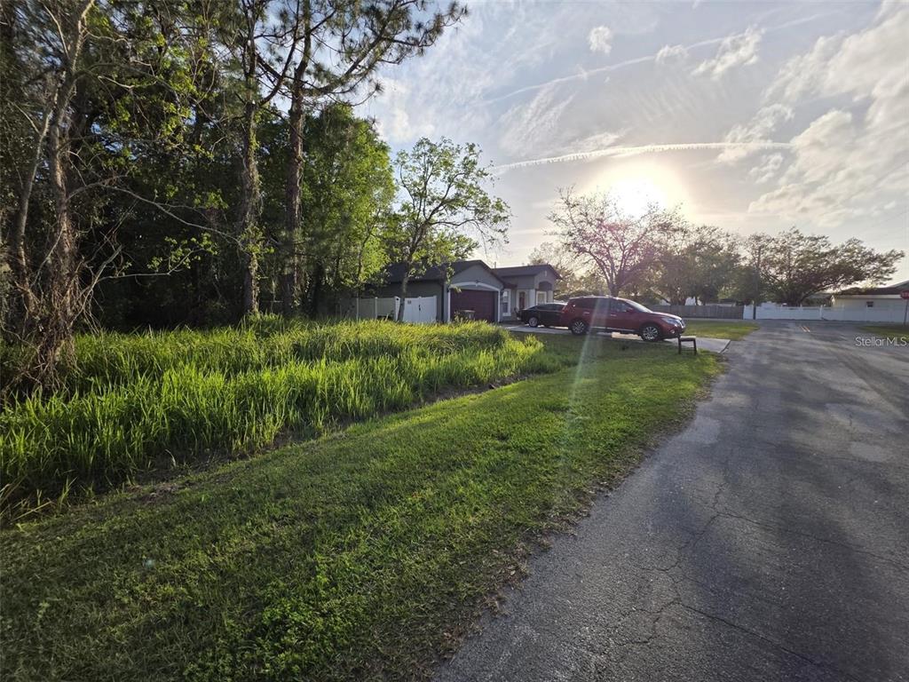 A view of a grassy lot next to a house with a parked car — CANNOCK DRIVE, KISSIMMEE, FL