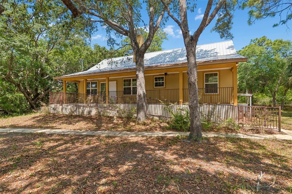 A one-story house with a metal roof and a wraparound porch sits among mature trees — 11274 S RIVIERA DRIVE, HOMOSASSA, FL