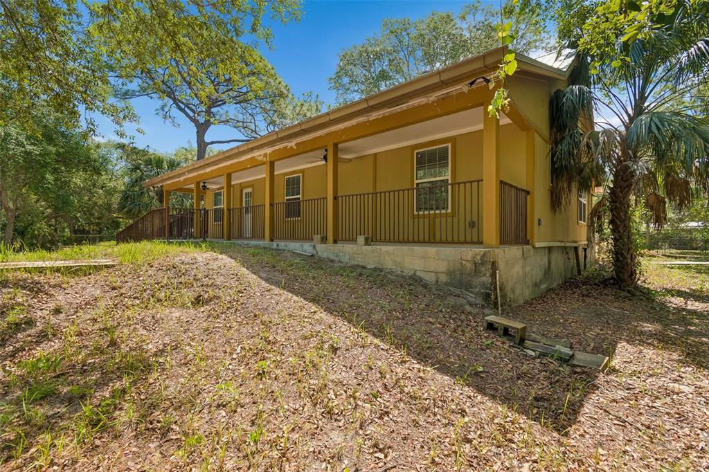 A tan house with a long covered porch and metal railing sits on a slope — 11274 S RIVIERA DRIVE, HOMOSASSA, FL