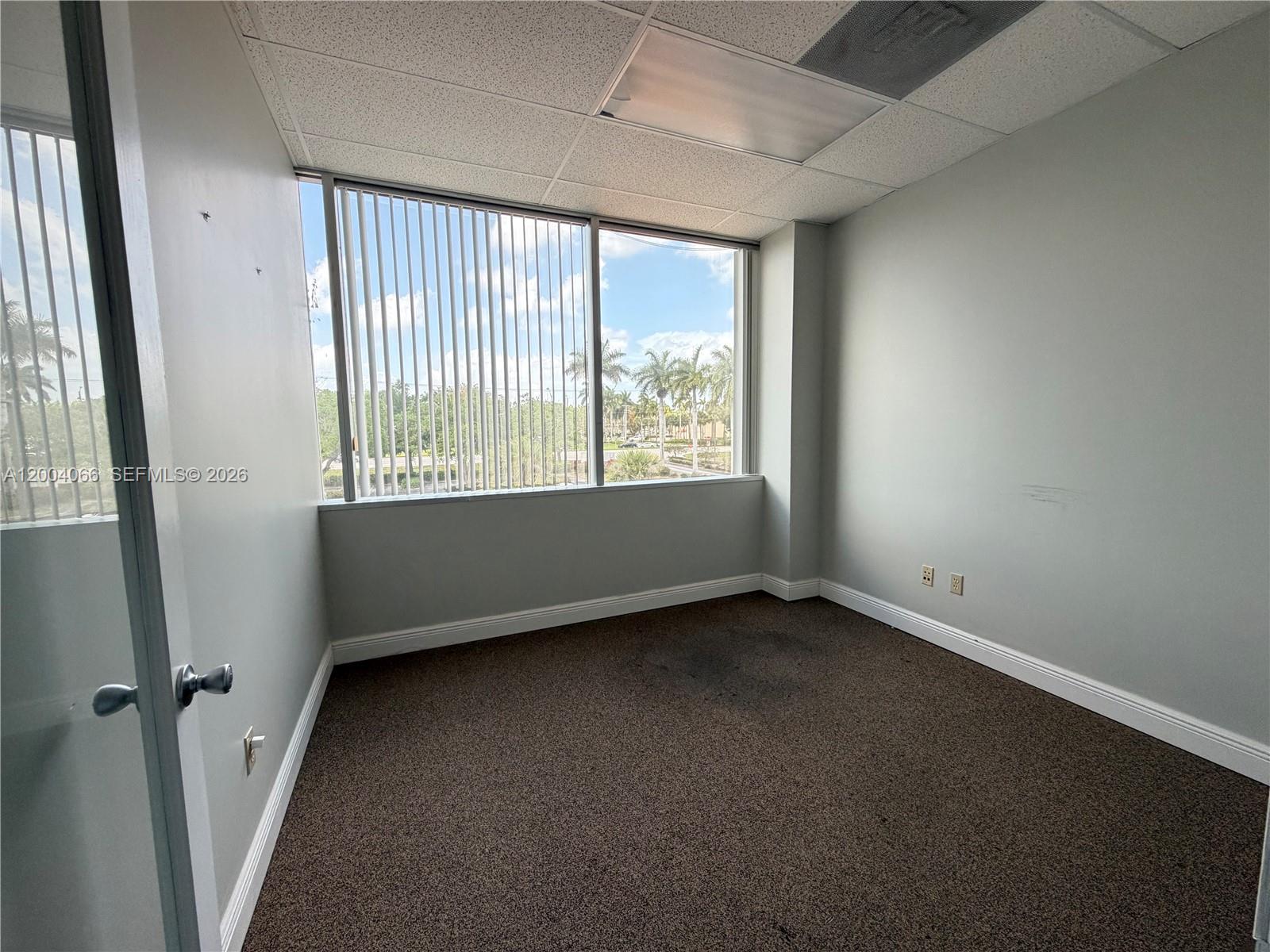 An empty office space features gray walls, brown carpet, and a large window with blinds — 4400 W Sample Rd # 230, Coconut Creek FL 33073, COCONUT CREEK, FL