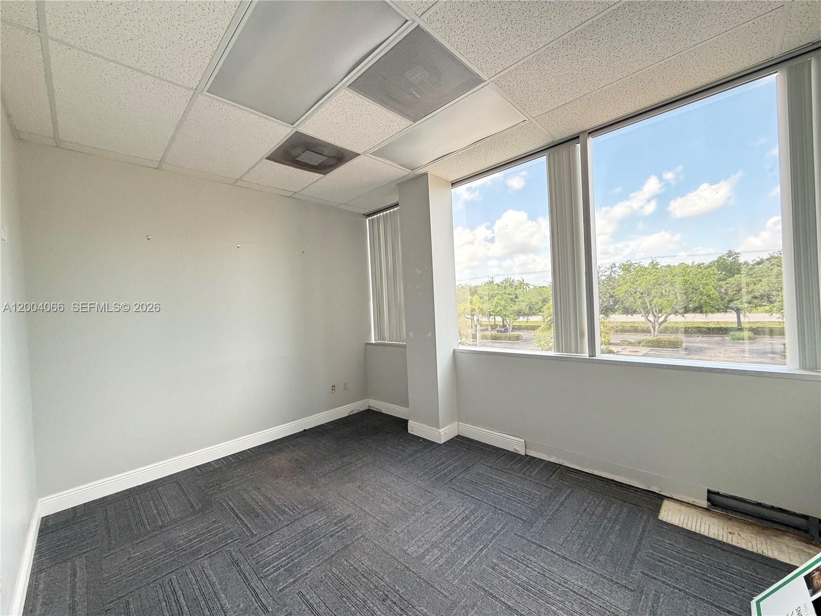 An empty office space features gray carpet, light-colored walls, and large windows with exterior views — 4400 W Sample Rd # 230, Coconut Creek FL 33073, COCONUT CREEK, FL