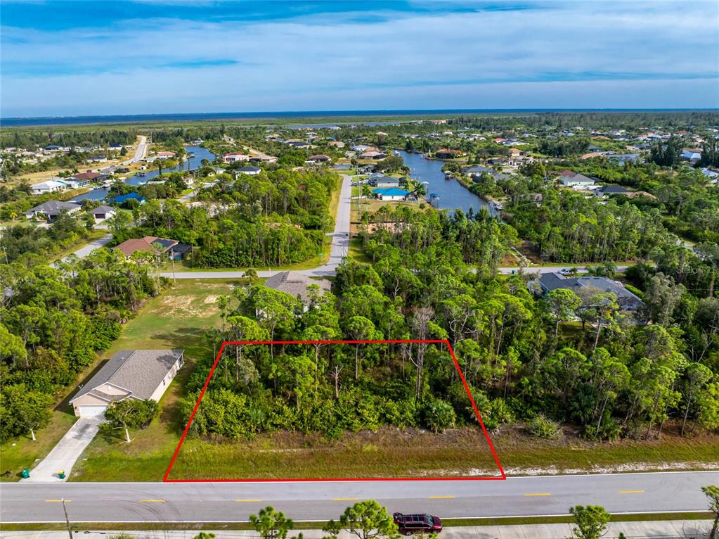 An aerial view shows a vacant, wooded residential lot outlined in red along a paved road — 9412 HALLENDALE DRIVE, PORT CHARLOTTE, FL