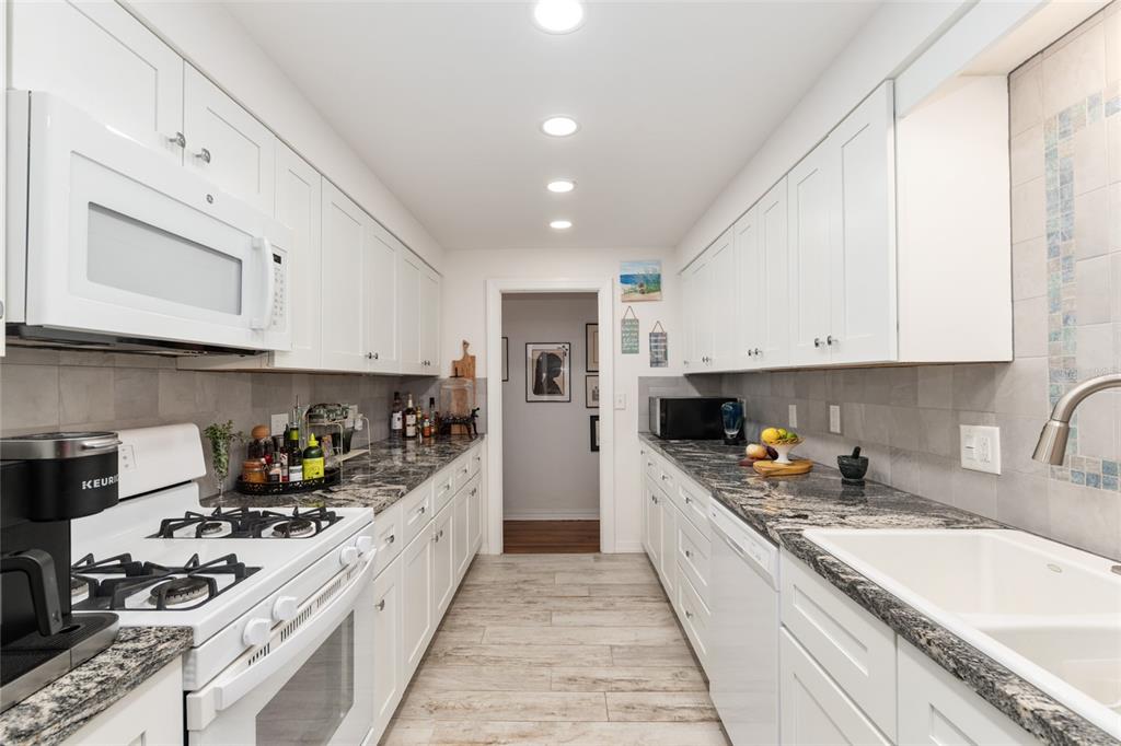 A galley kitchen features white cabinets, dark granite countertops, and light wood-look tile flooring — 1210 SE 14TH AVENUE, OCALA, FL