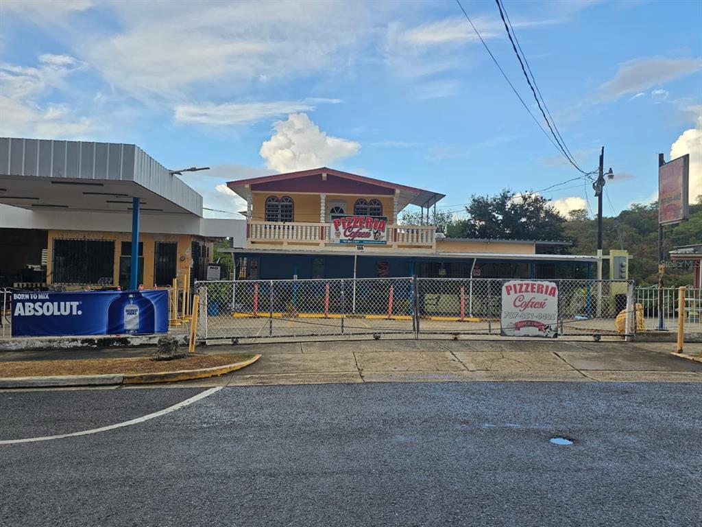 A two-story building with a pizzeria sign stands behind a chain-link fence and gas station — Carr. 307, Km. 5.2 BARRIO PEDERNALES, CABO ROJO, PR