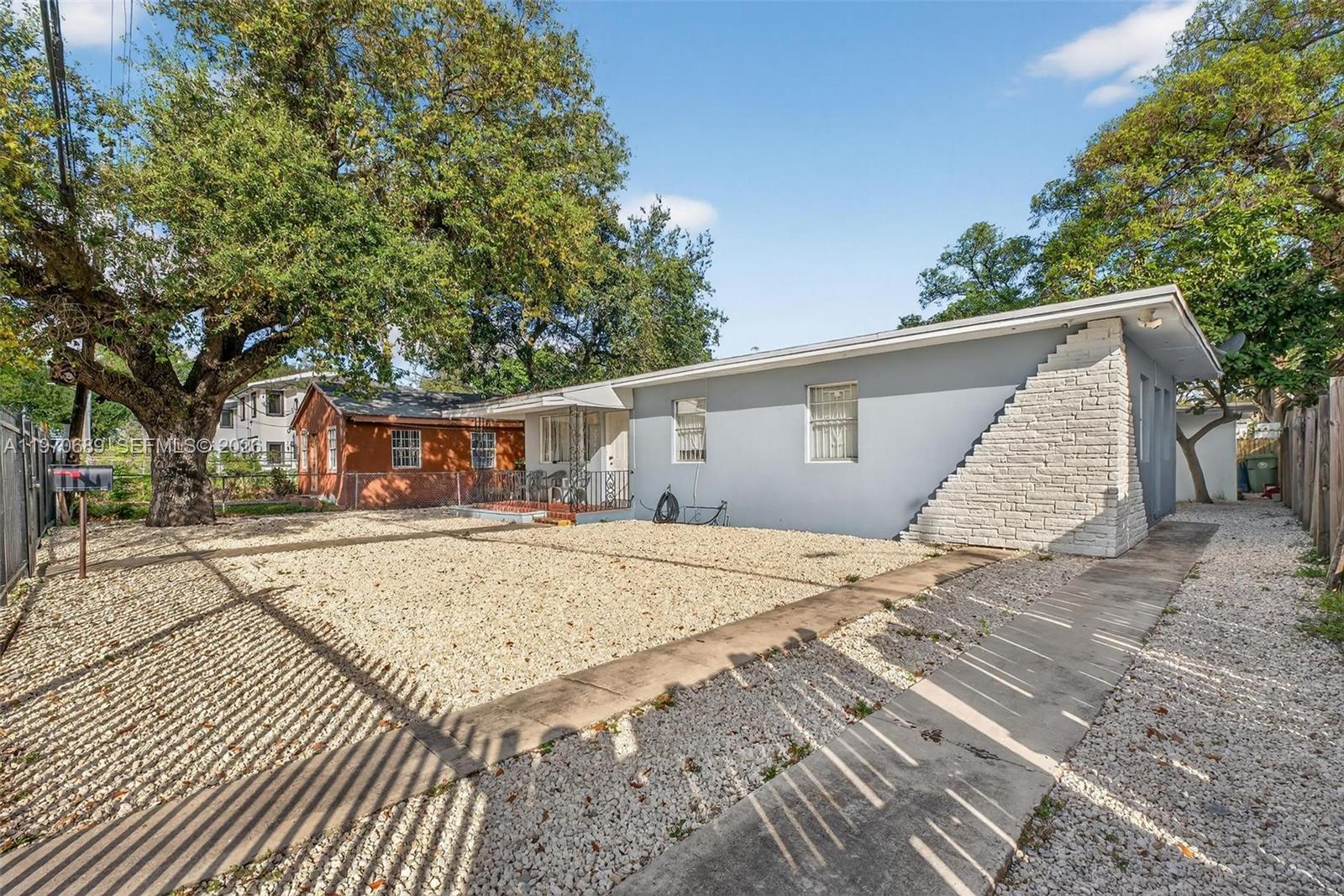 A gray house with a stone-accented wall sits behind a gravel yard and concrete path — 2741 NW 43rd Ter, Miami FL 33142, MIAMI, FL