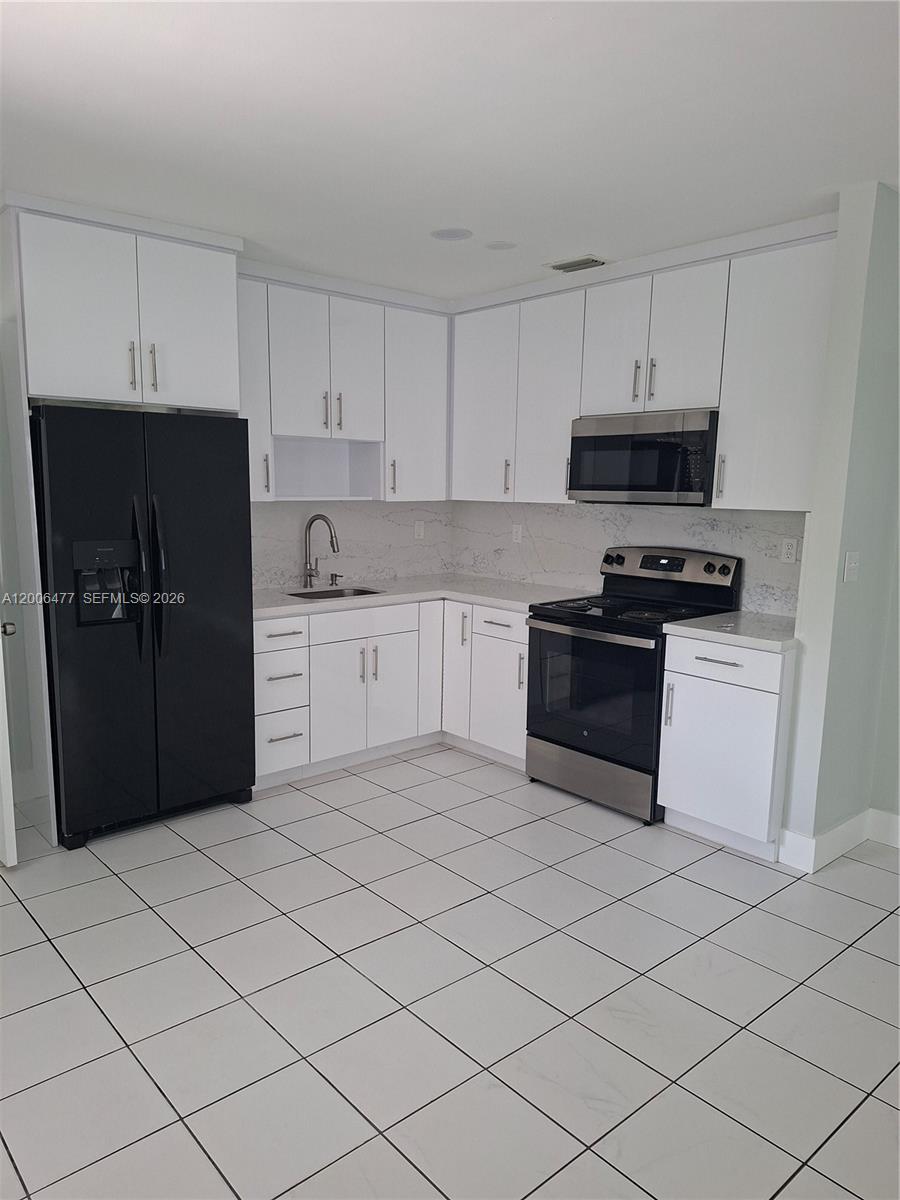 A kitchen features white cabinets, stainless steel appliances, a black refrigerator, and white tile flooring — 1814 SW 97th Terrace # A, Miramar FL 33025, MIRAMAR, FL
