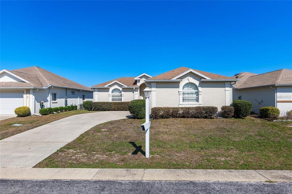 A single-story suburban house with a tan stucco exterior, brown roof, and a concrete driveway — 5891 NW 26TH STREET, OCALA, FL
