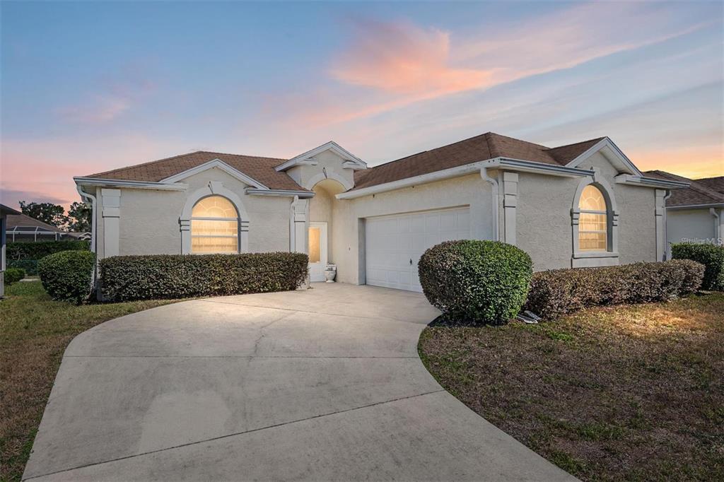 A single-story stucco house with a two-car garage and arched windows at sunset — 5891 NW 26TH STREET, OCALA, FL