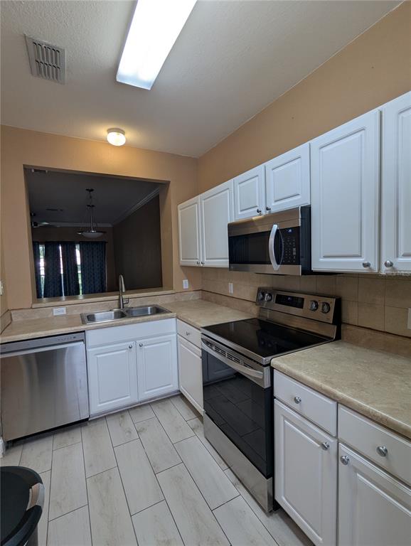 A kitchen features white cabinets, stainless steel appliances, tan countertops, and light-colored tile flooring — 4872 NW 42ND ROAD UNIT 103, GAINESVILLE, FL