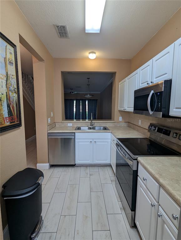 A galley kitchen features white cabinets, stainless steel appliances, and light-colored wood-look tile flooring — 4872 NW 42ND ROAD UNIT 103, GAINESVILLE, FL