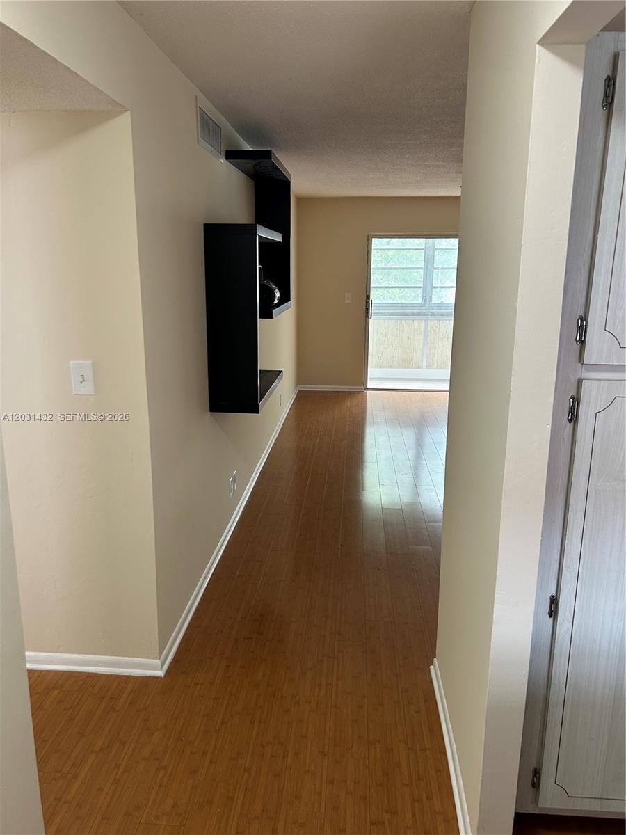 A hallway with light wood flooring leads toward a glass door opening to a balcony — 218 NE 12th Ave # 203, Hallandale Beach FL 33009, HALLANDALE BEACH, FL