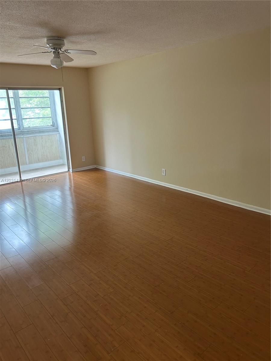An empty room features light-colored walls, wood-look flooring, a ceiling fan, and a sliding glass door — 218 NE 12th Ave # 203, Hallandale Beach FL 33009, HALLANDALE BEACH, FL