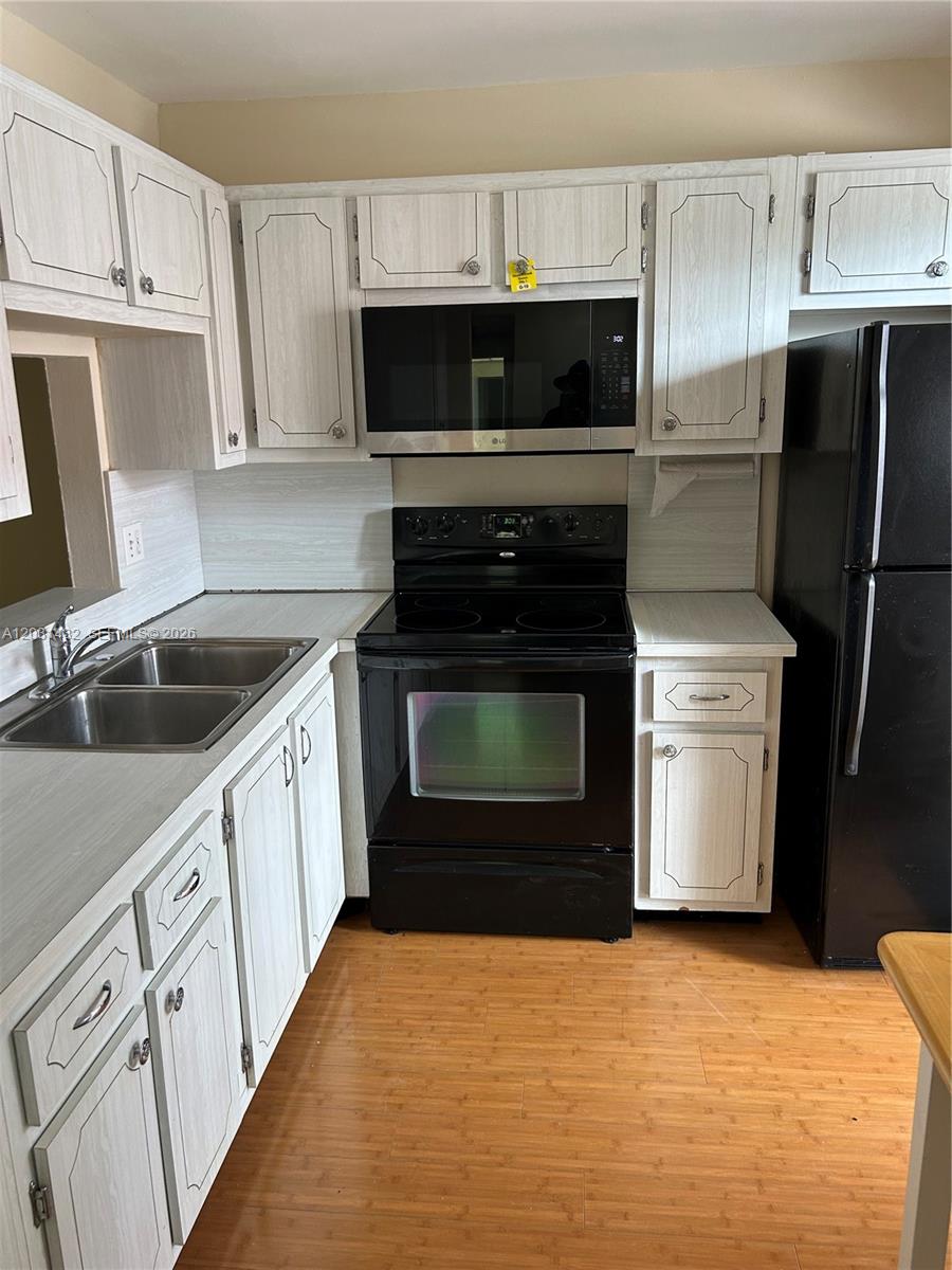 A kitchen features light wood-grain cabinets, black appliances, and a double stainless steel sink — 218 NE 12th Ave # 203, Hallandale Beach FL 33009, HALLANDALE BEACH, FL