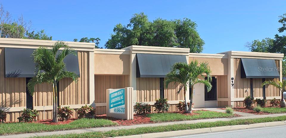 A single-story commercial building with tan vertical siding, dark awnings, and palm trees in front — 917 EMMETT STREET, KISSIMMEE, FL