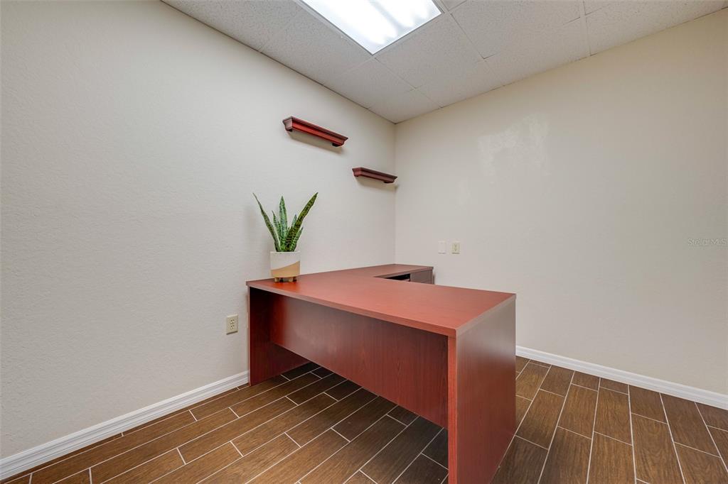An office space features a wooden L-shaped desk, a potted plant, and wood-look tile flooring — 917 EMMETT STREET, KISSIMMEE, FL