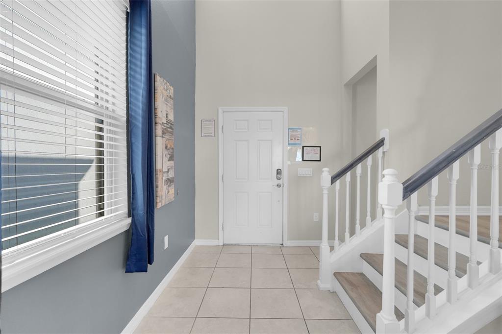 A tiled entryway features a white front door, high ceilings, and a staircase with railings — 2440 TANGIER DRIVE, KISSIMMEE, FL