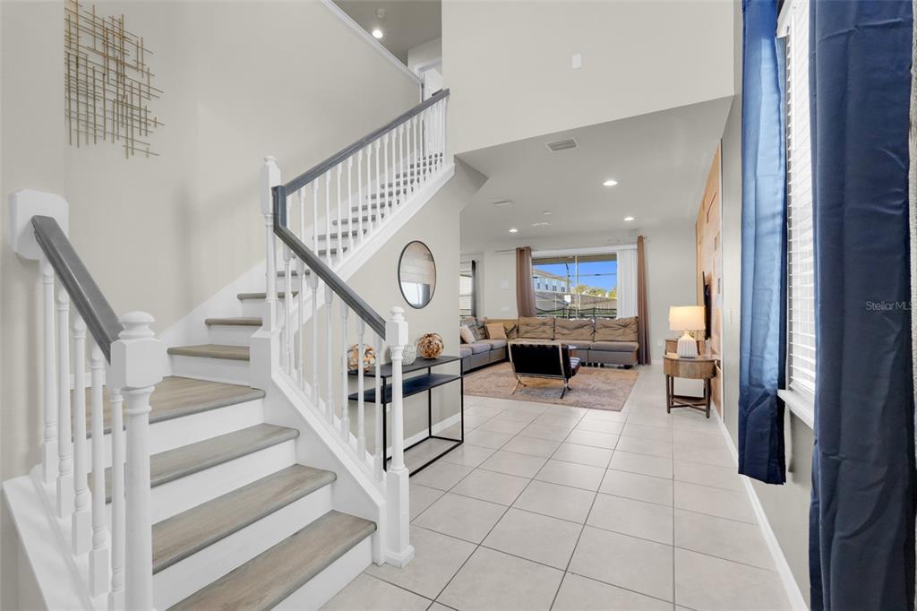 A foyer with a staircase leads into a living room featuring tile floors and furniture — 2440 TANGIER DRIVE, KISSIMMEE, FL