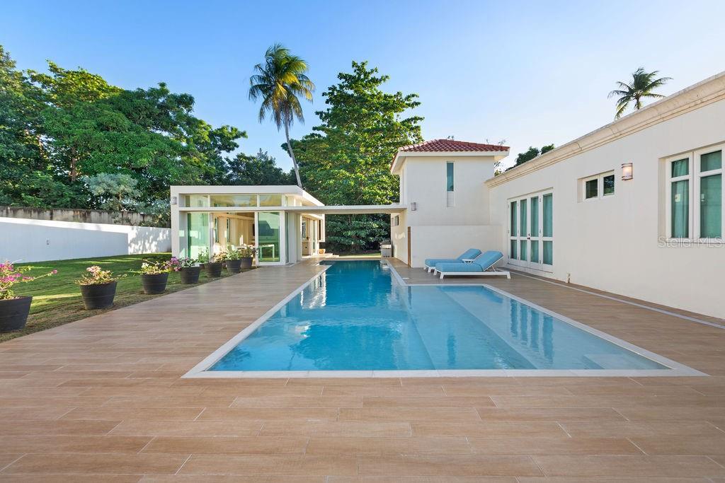 A rectangular swimming pool sits between a modern glass-walled structure and a white house — 251 DORADO BEACH EAST, DORADO, PR