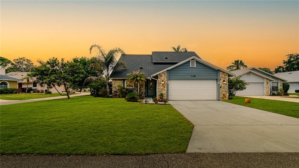 A single-story house with a stone facade, blue siding, and a two-car garage at sunset — 108 GREBE COURT, DAYTONA BEACH, FL